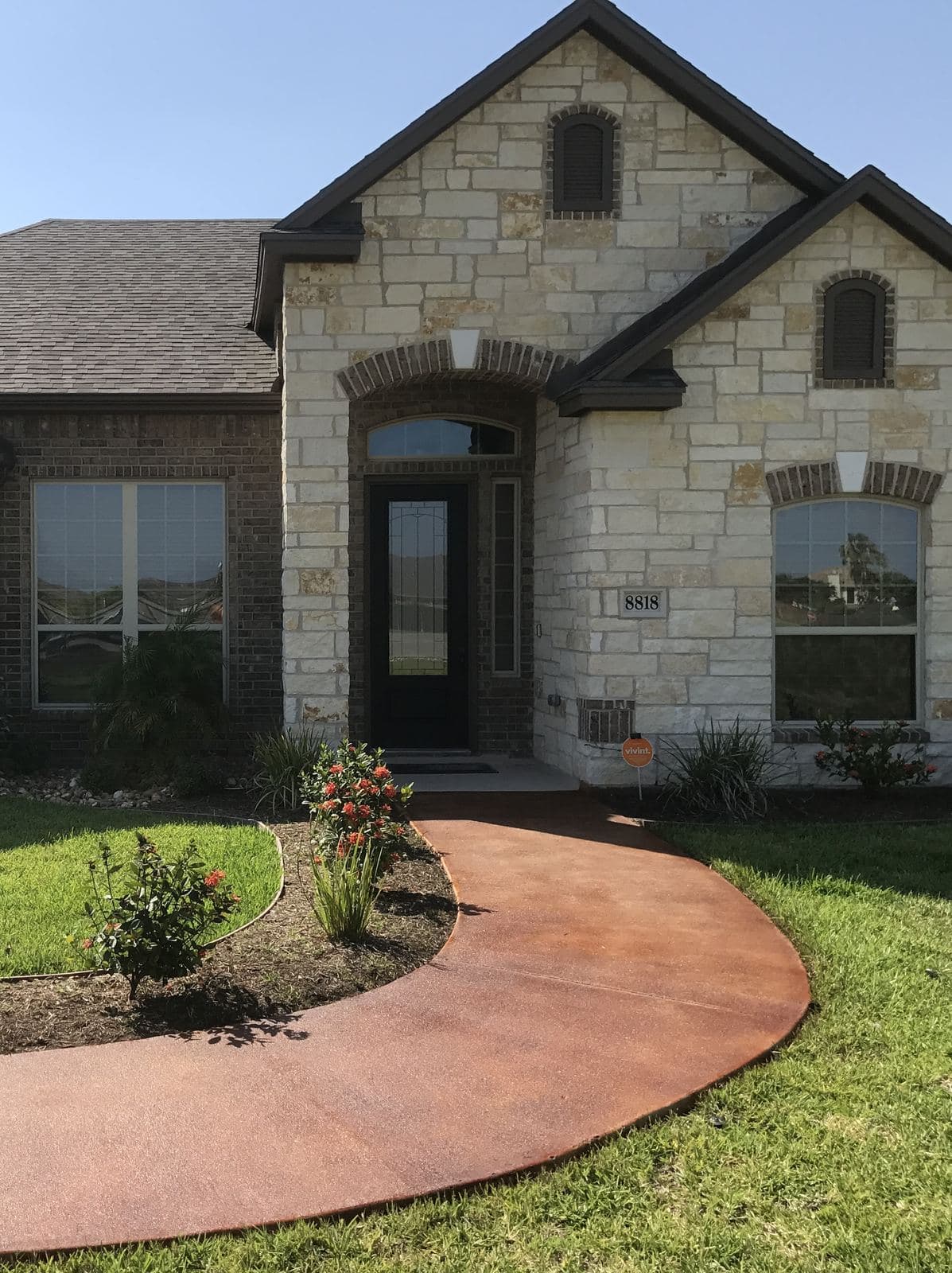 Curved red acid-stained front walkway leading to a stone home