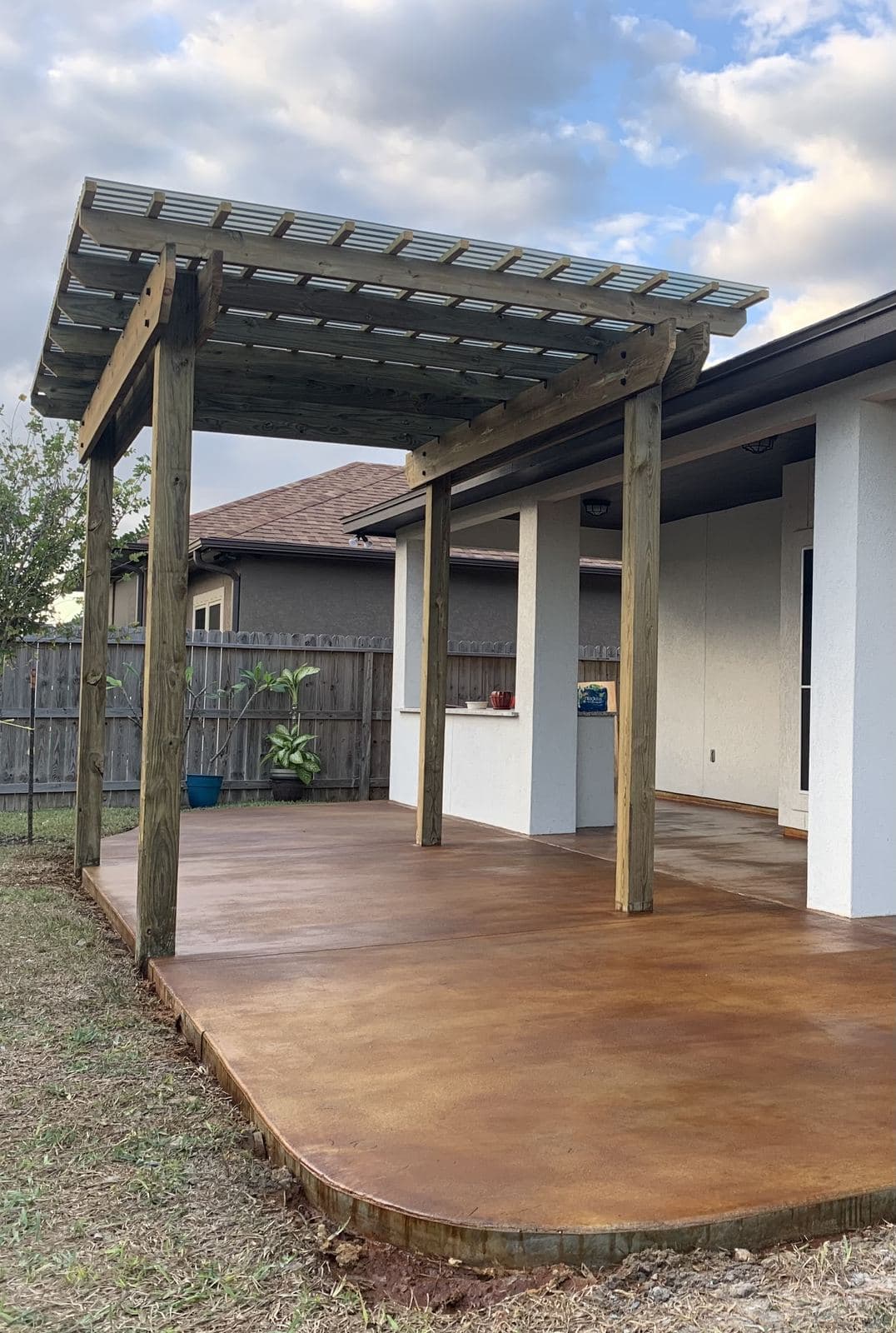 Curved acid-stained patio under a cedar pergola beside a white home
