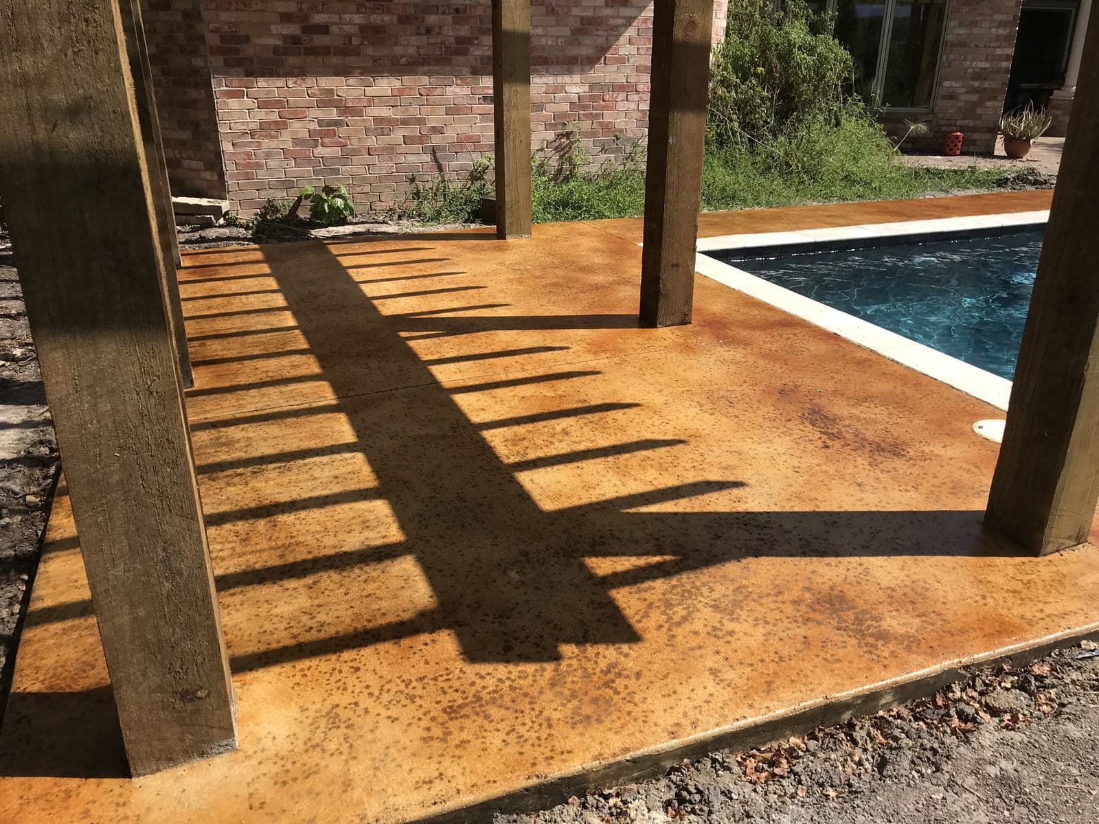 Amber acid-stained pool deck under a cedar pergola casting shadows