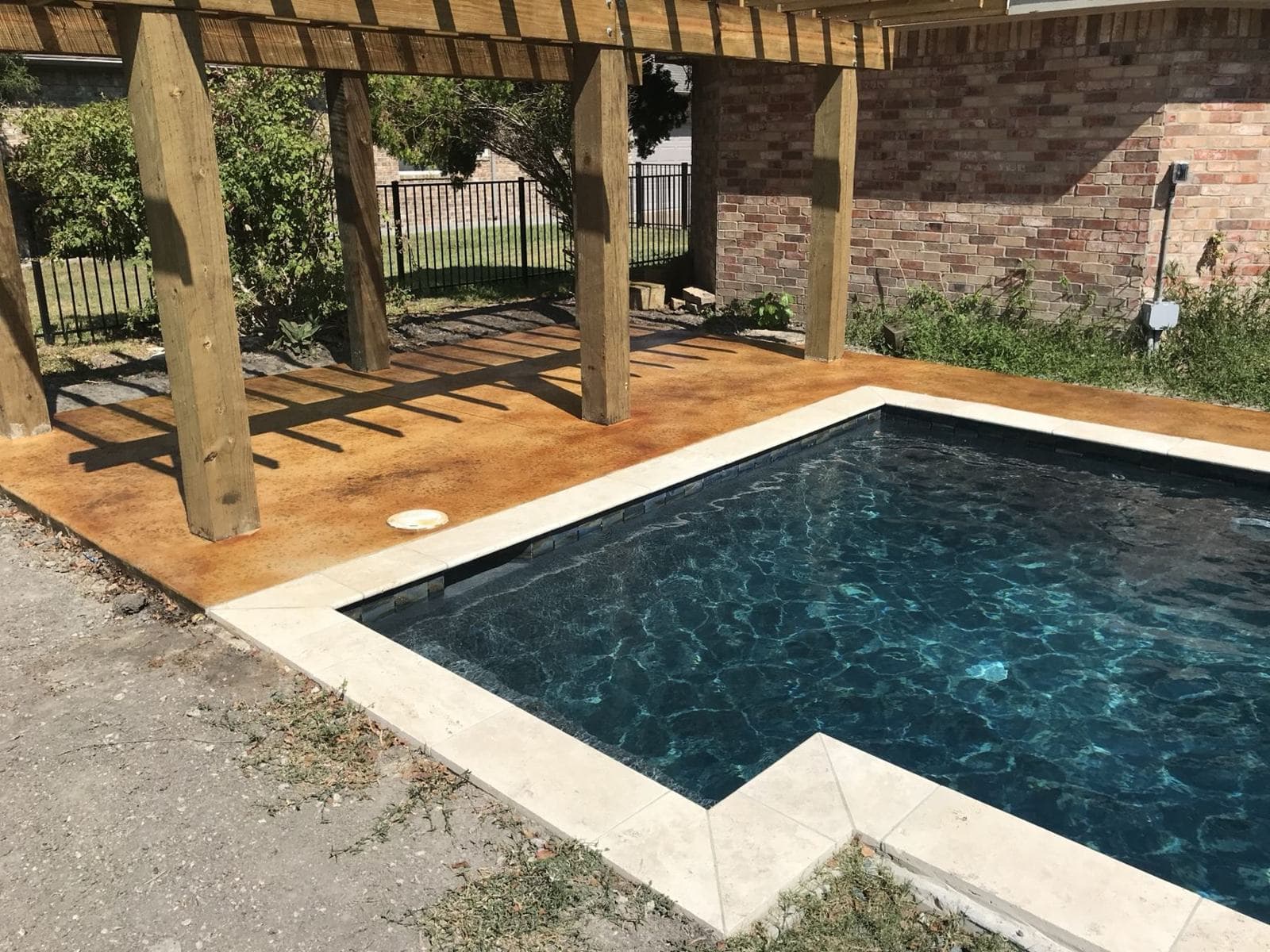 Acid-stained pool deck with a cedar pergola casting shadows across the concrete
