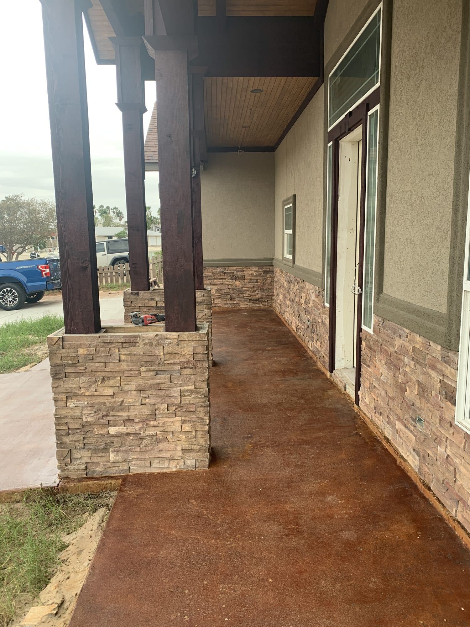 Burnt-orange acid-stained walkway between a stucco home and stone columns
