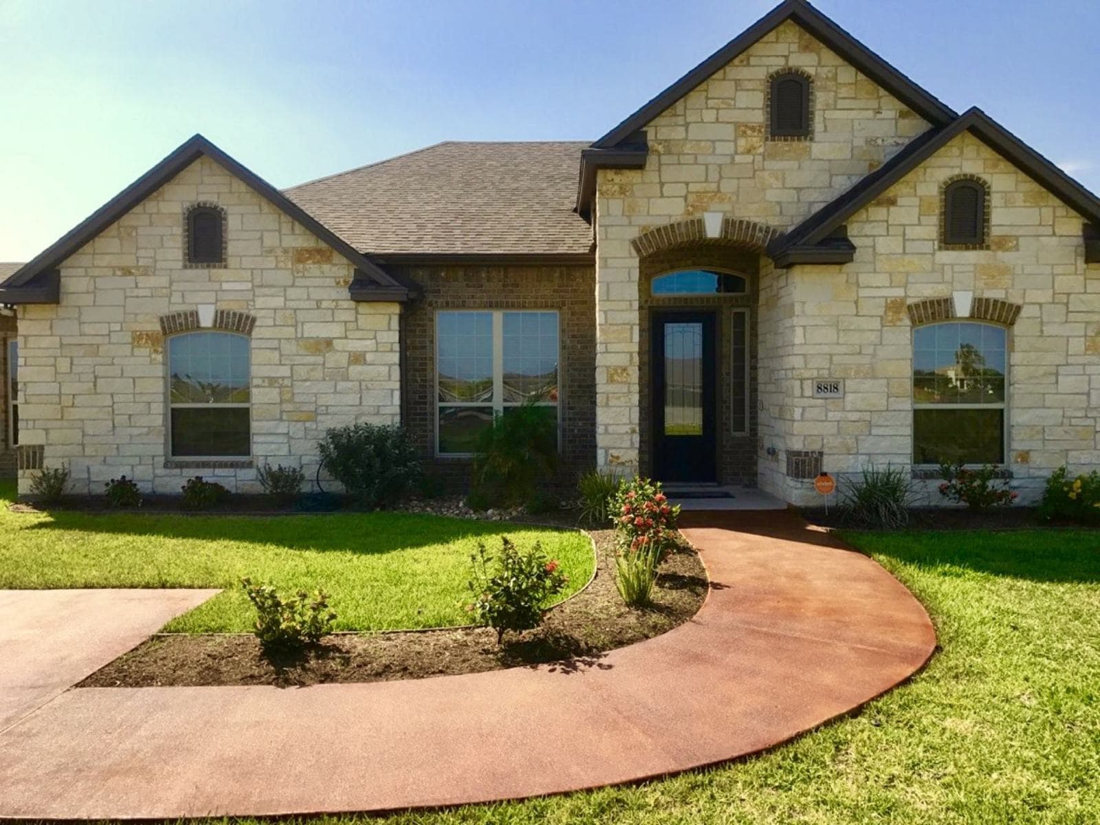 Curved acid-stained concrete walkway leading to a stone front entry