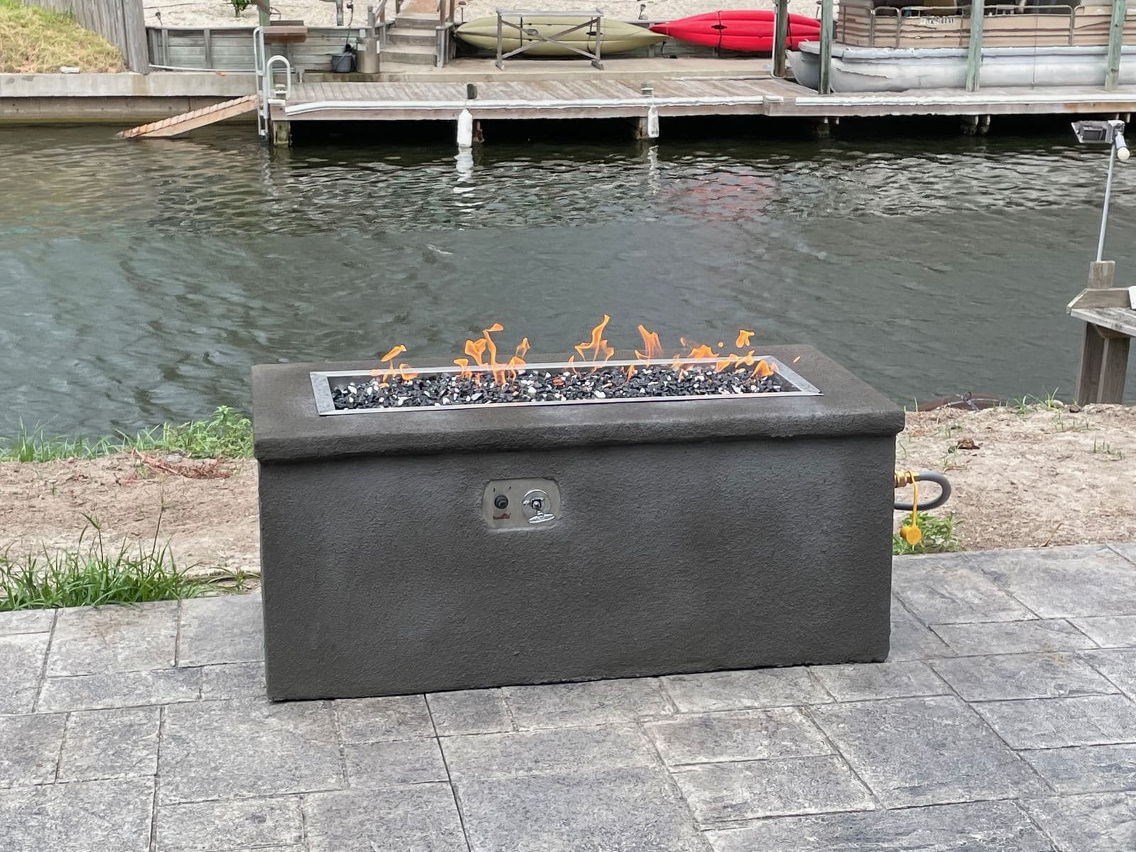 Rectangular gas fire table on a stamped concrete patio by a canal