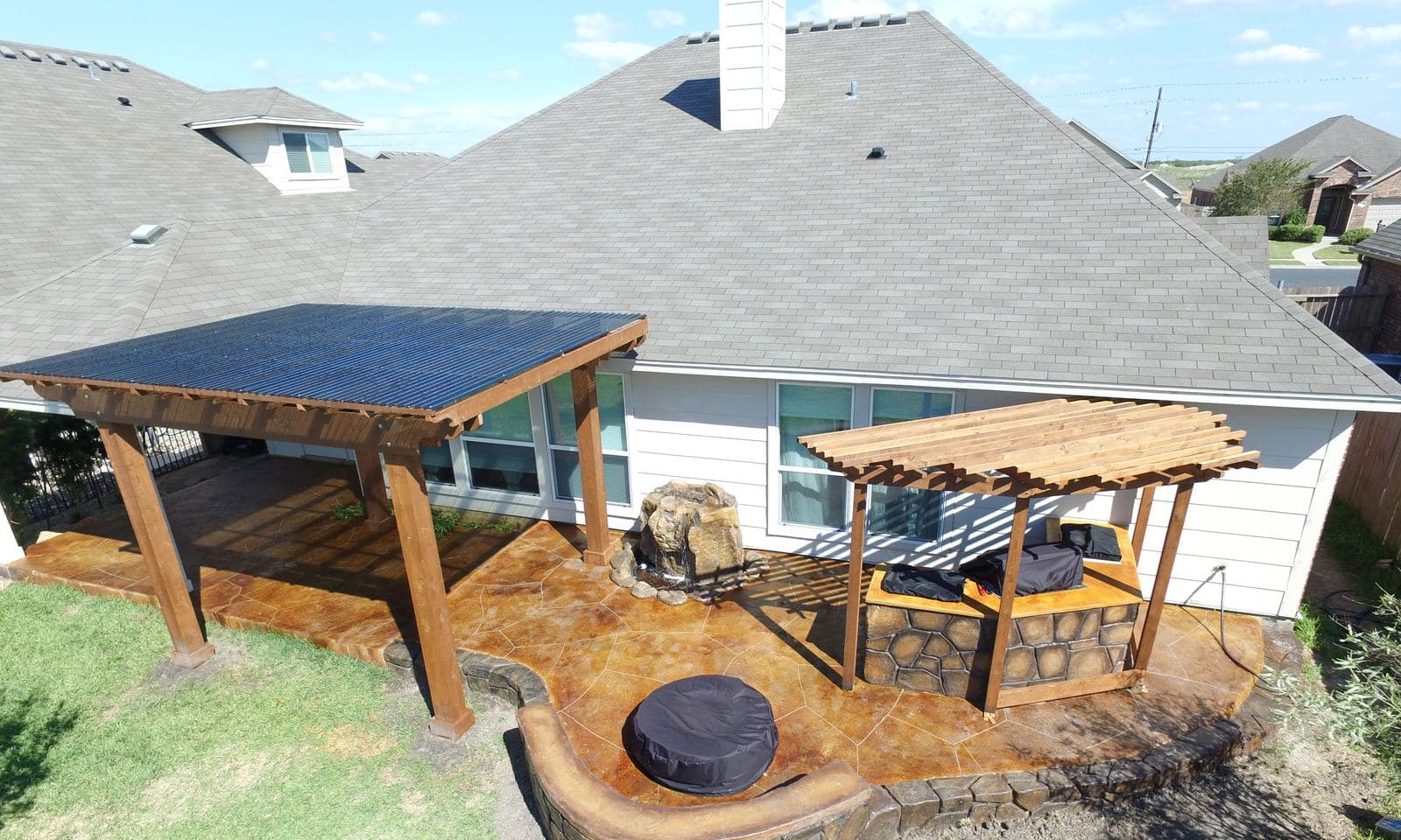 Aerial view of a stained patio with two pergolas, a seat wall and a round fire pit