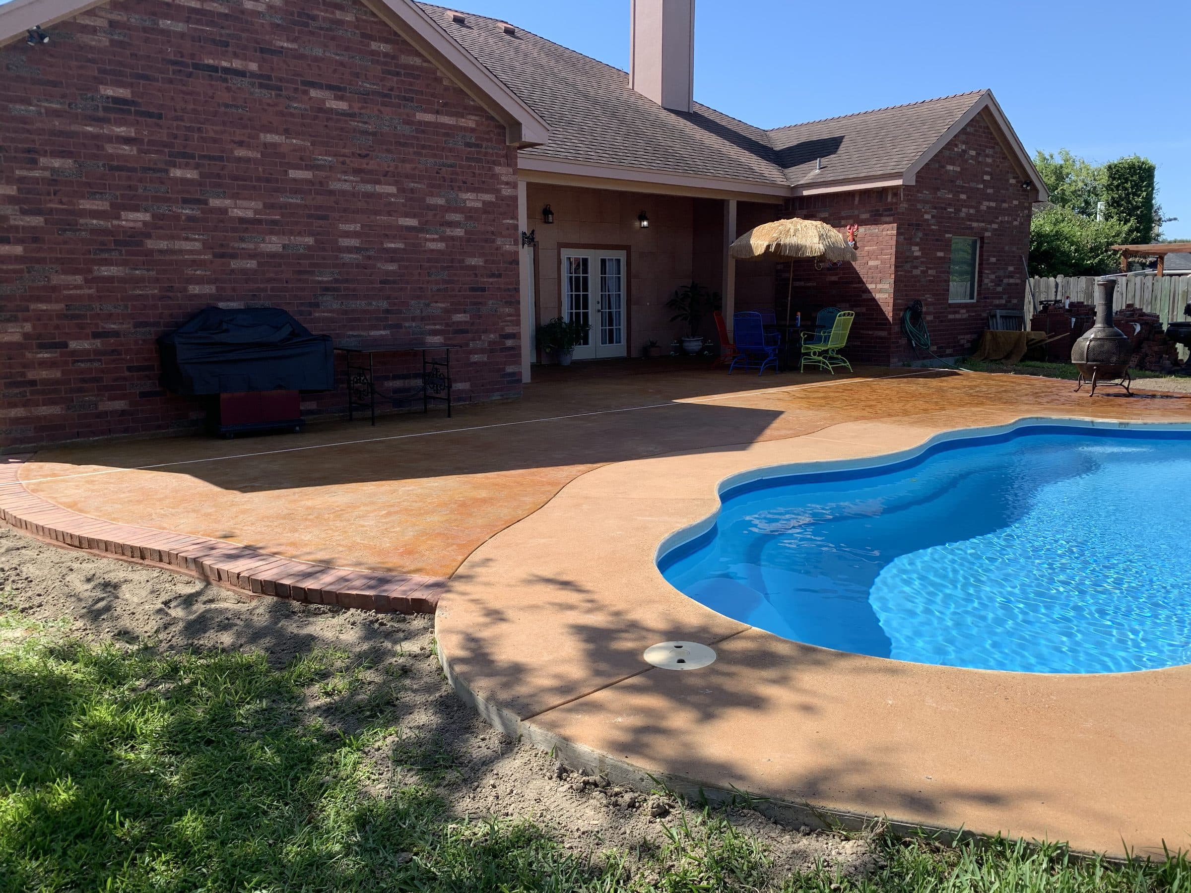 Freeform pool deck resurfaced with a tan stained concrete overlay and brick border