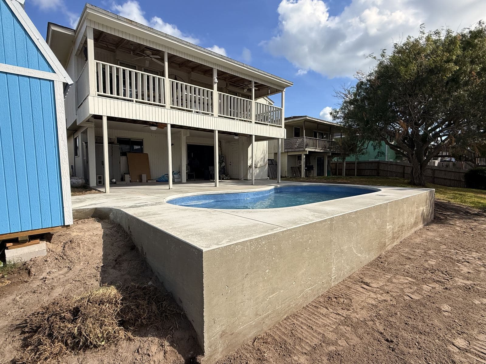 Raised fiberglass pool with a concrete wall behind a raised coastal home
