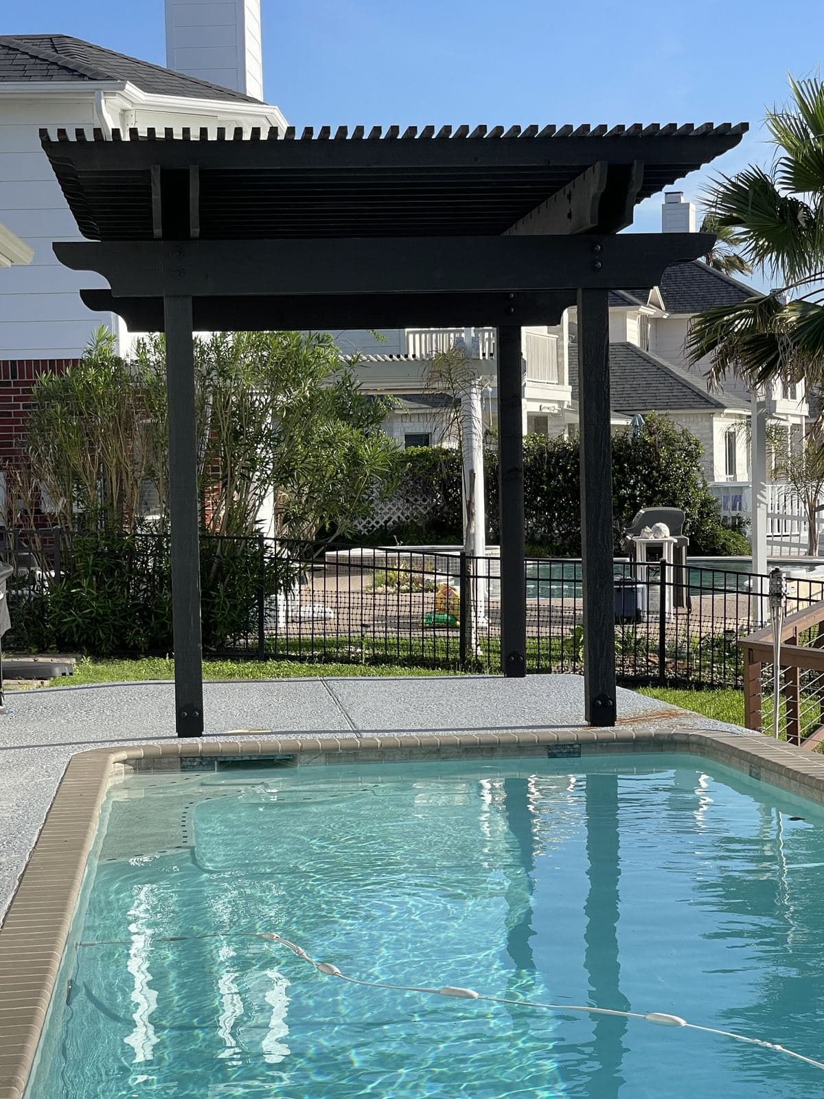 Black pergola at the end of a backyard pool