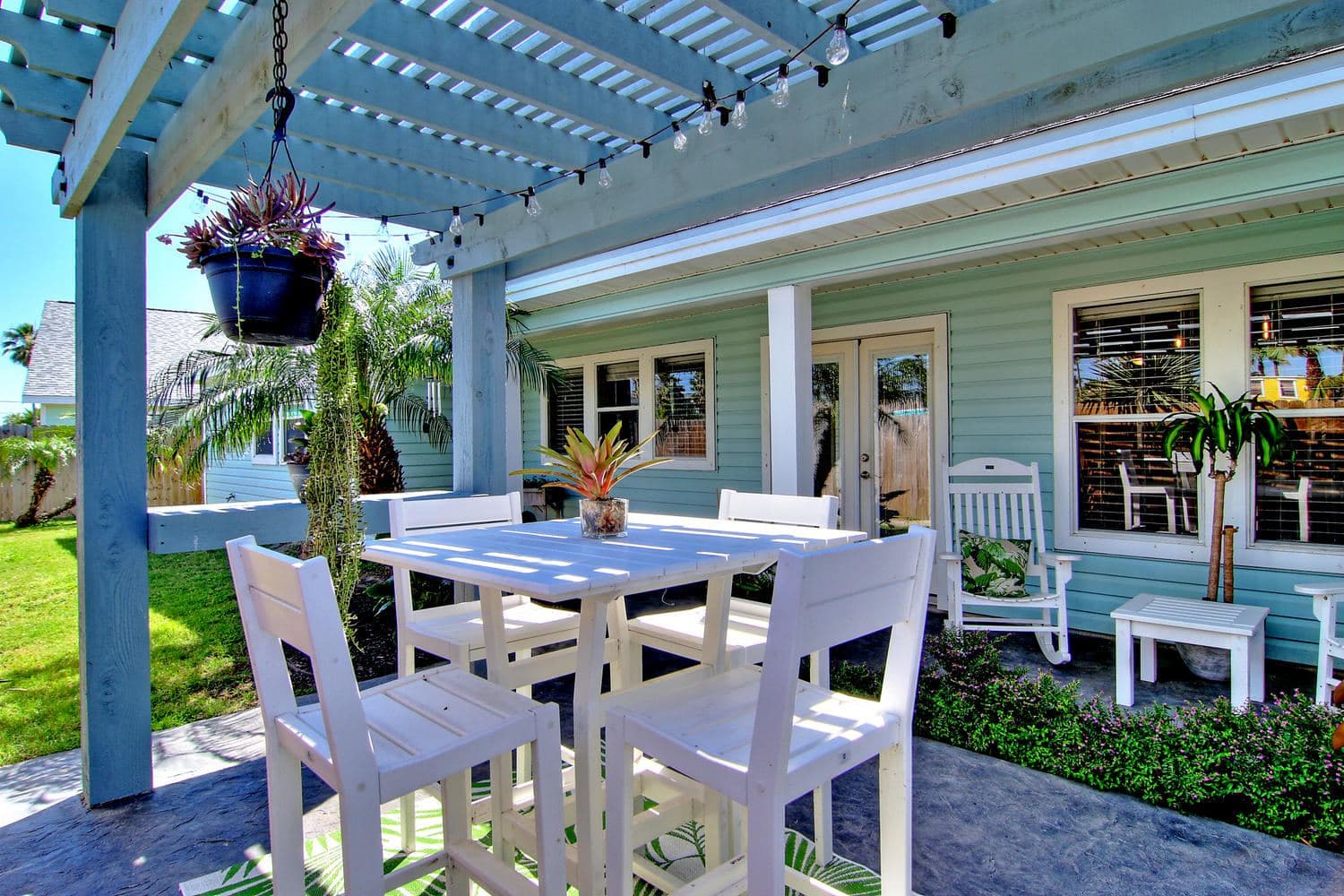 Blue pergola over a patio dining set with a hanging flower basket