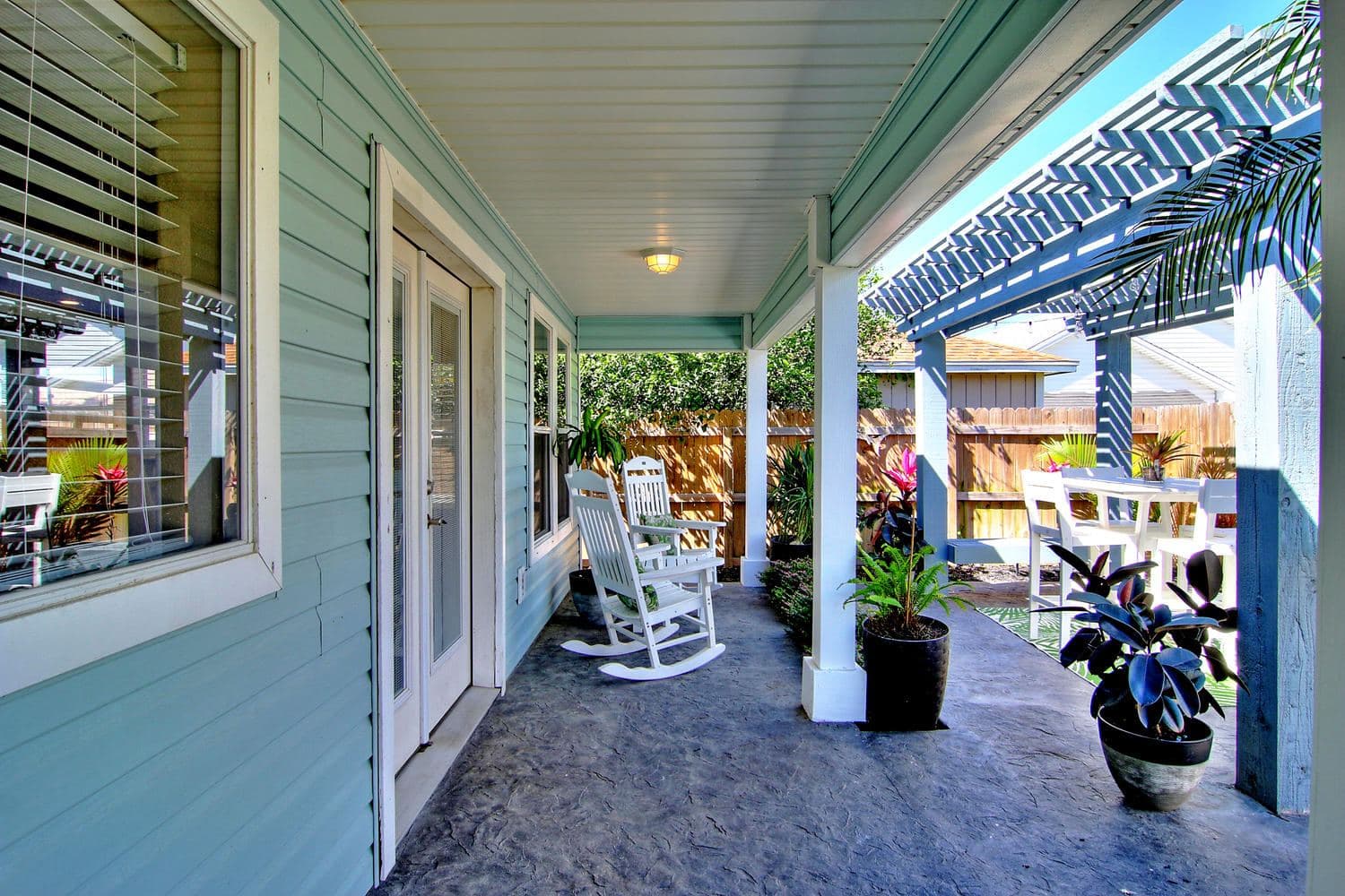 Blue pergola extending off a covered porch with rocking chairs