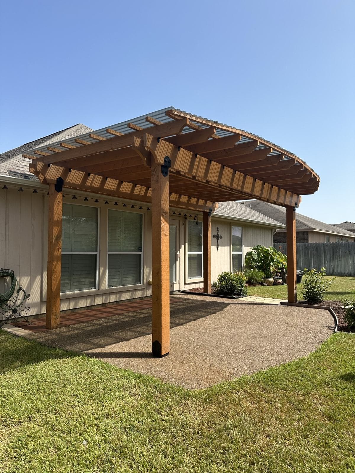 Freestanding cedar pergola with arched beams over a concrete patio