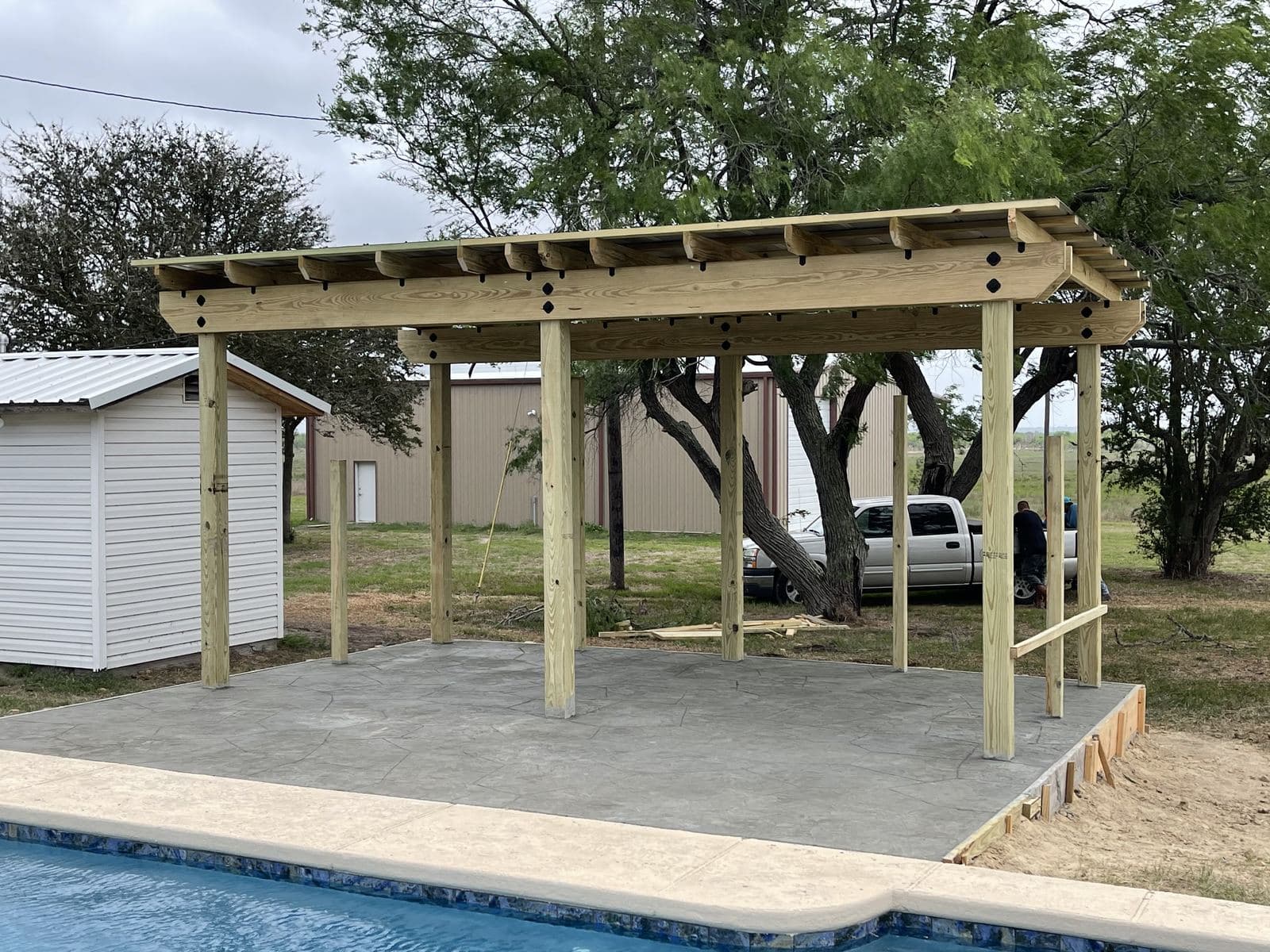 Open pergola over a new concrete slab at the edge of a pool