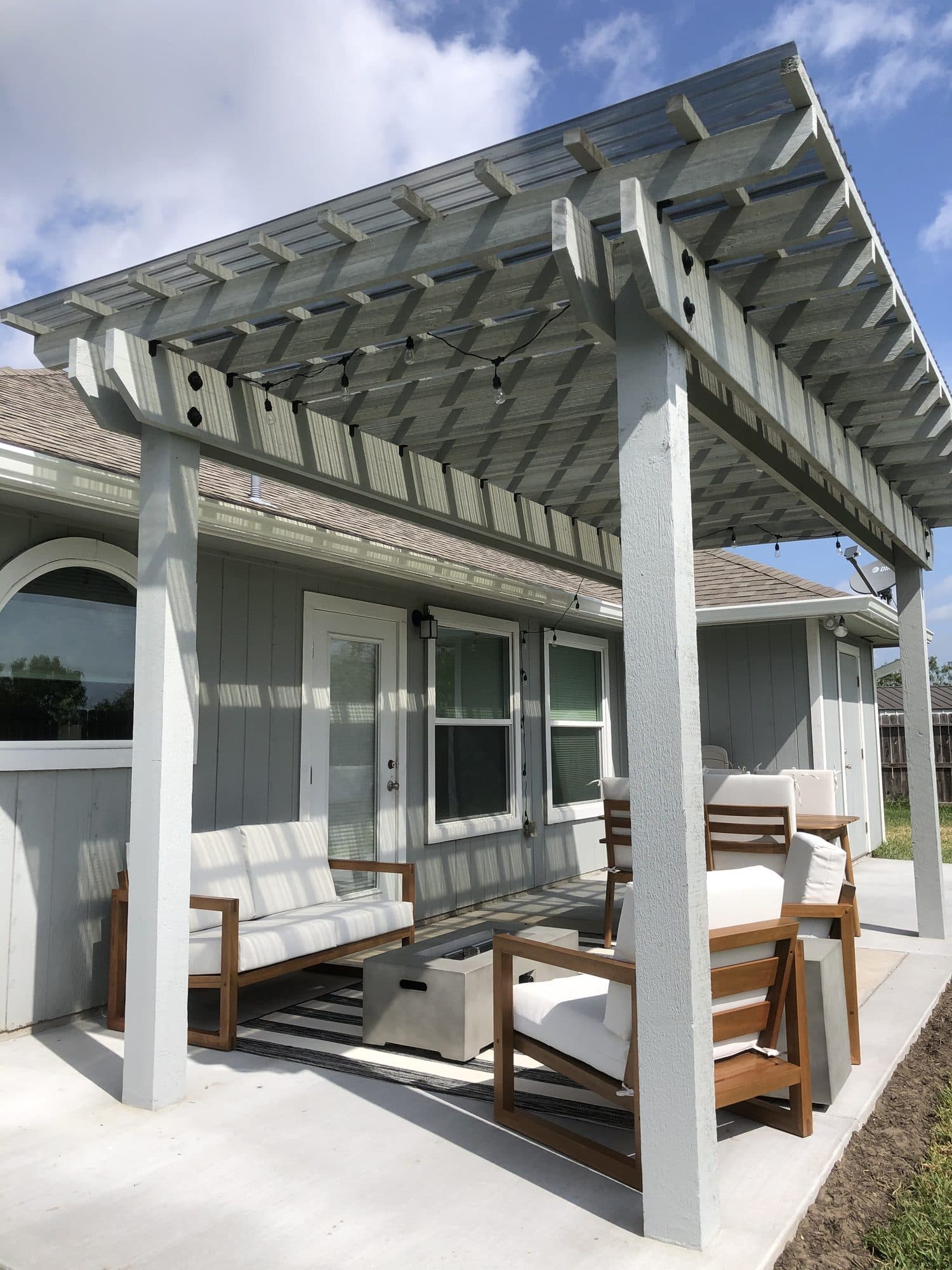 White attached pergola shading a back patio with outdoor seating