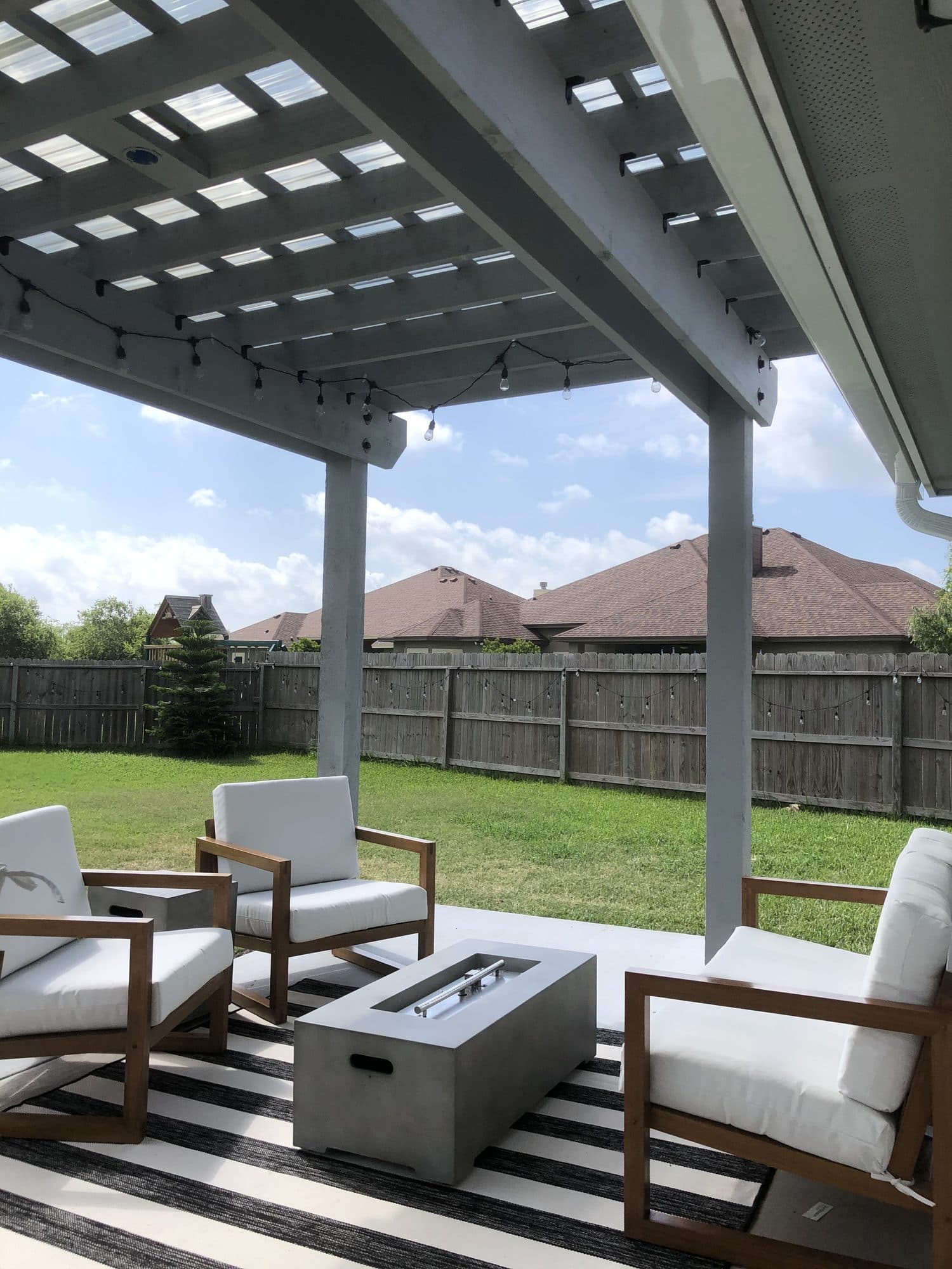 White pergola over a patio with lounge chairs and a fire table