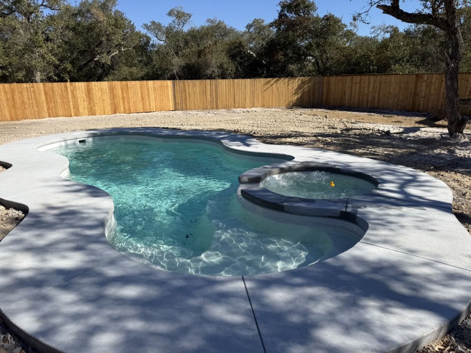 New fiberglass pool with a poured concrete deck in a fenced backyard