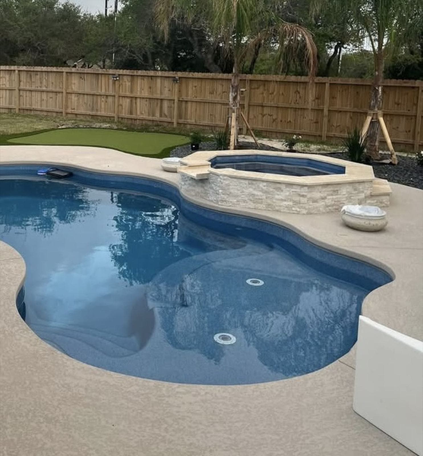 Freeform fiberglass pool and spa with a light broom-finished concrete deck