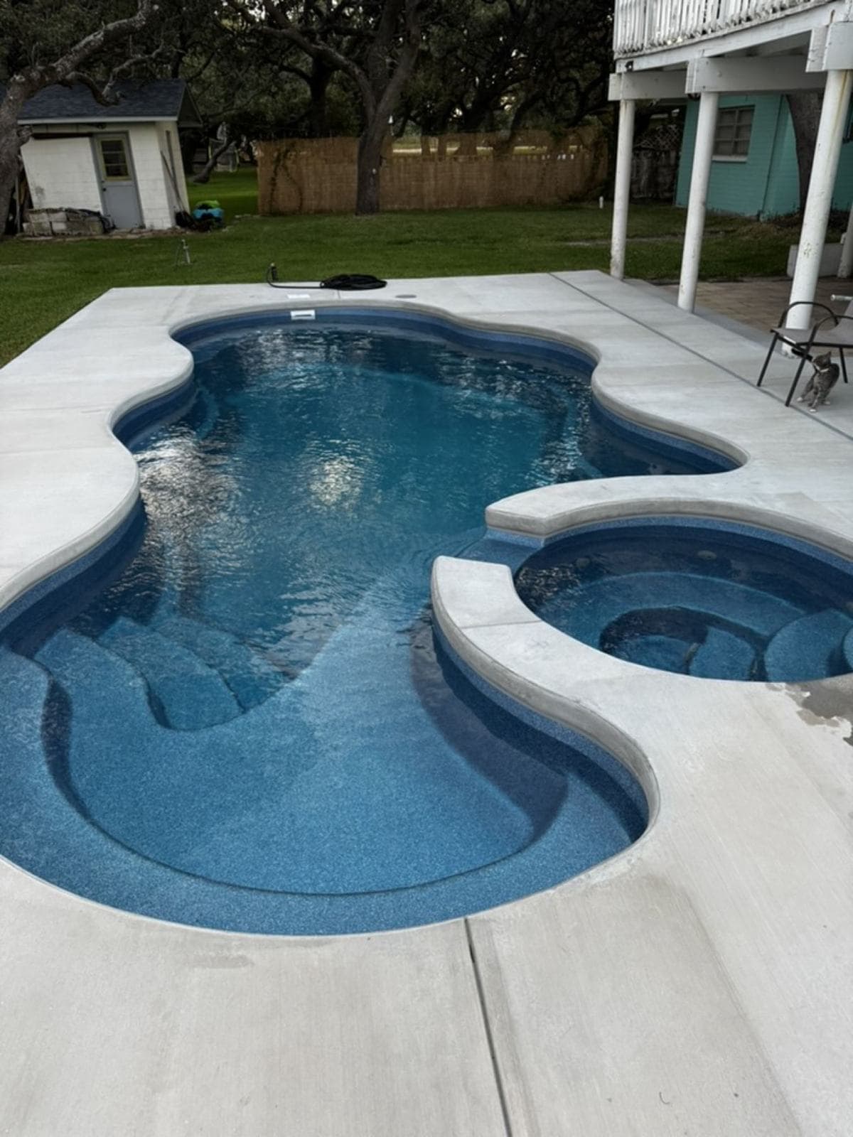 Fiberglass pool with raised spa and a clean concrete deck beside a two-story home