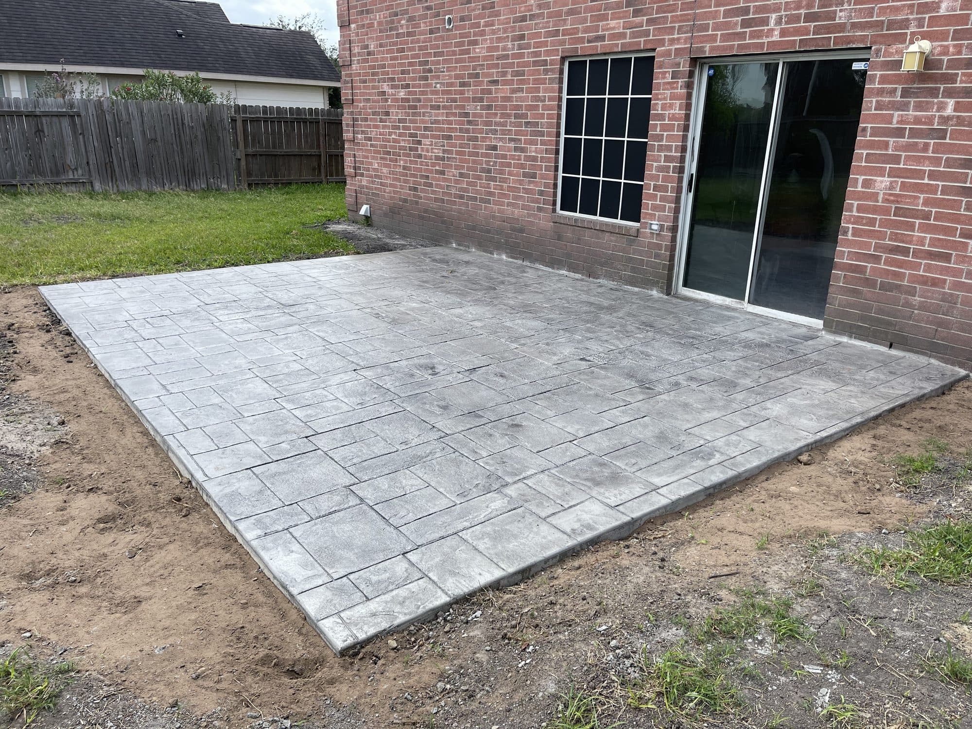Light-gray ashlar-pattern stamped patio behind a brick home