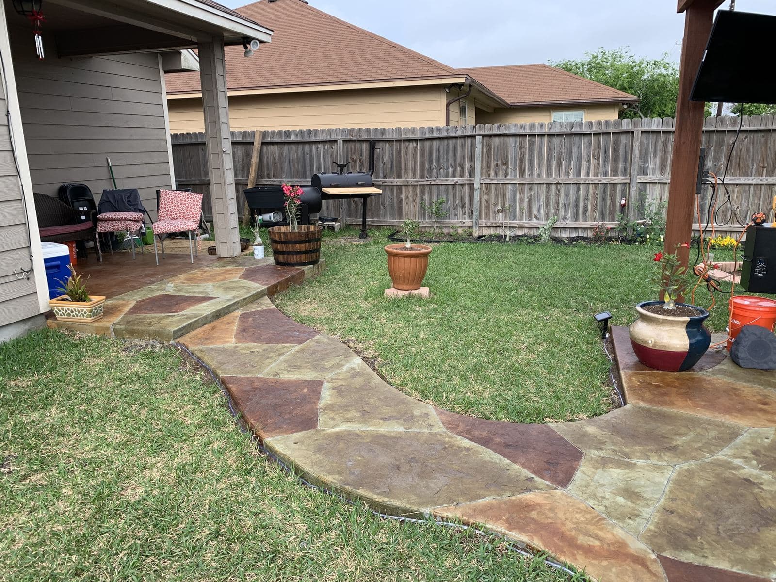 Curving stamped flagstone walkway through a back yard to a covered patio