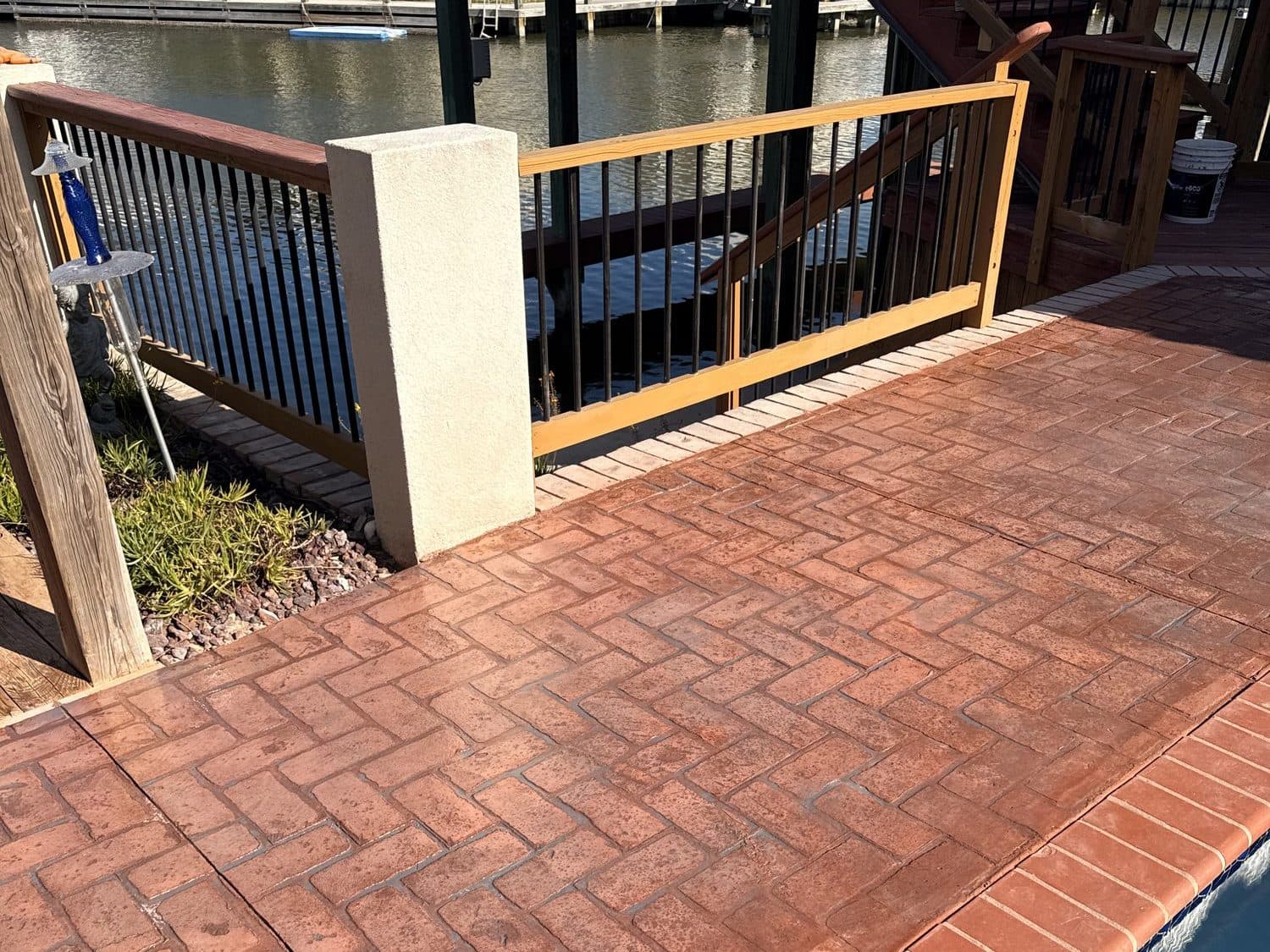 Finished red herringbone brick-pattern stamped deck beside a pool, with a railing and canal behind