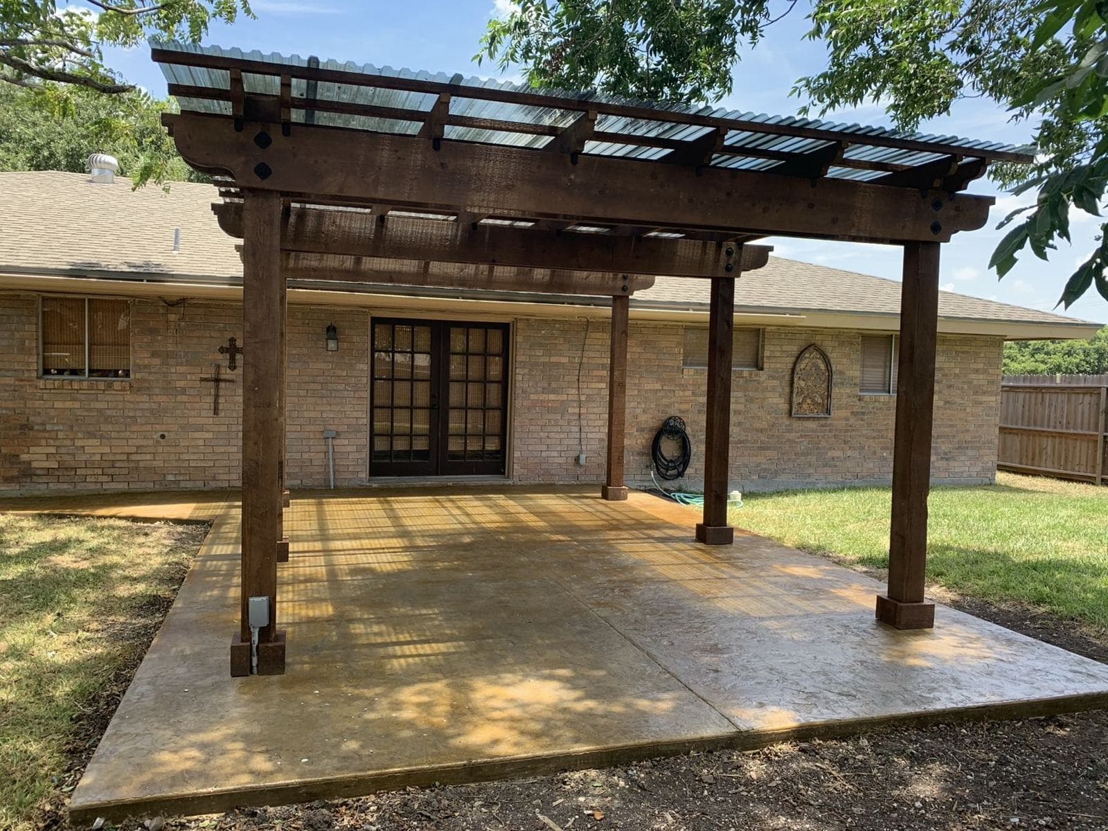 Stamped concrete patio with a wooden pergola behind a brick home