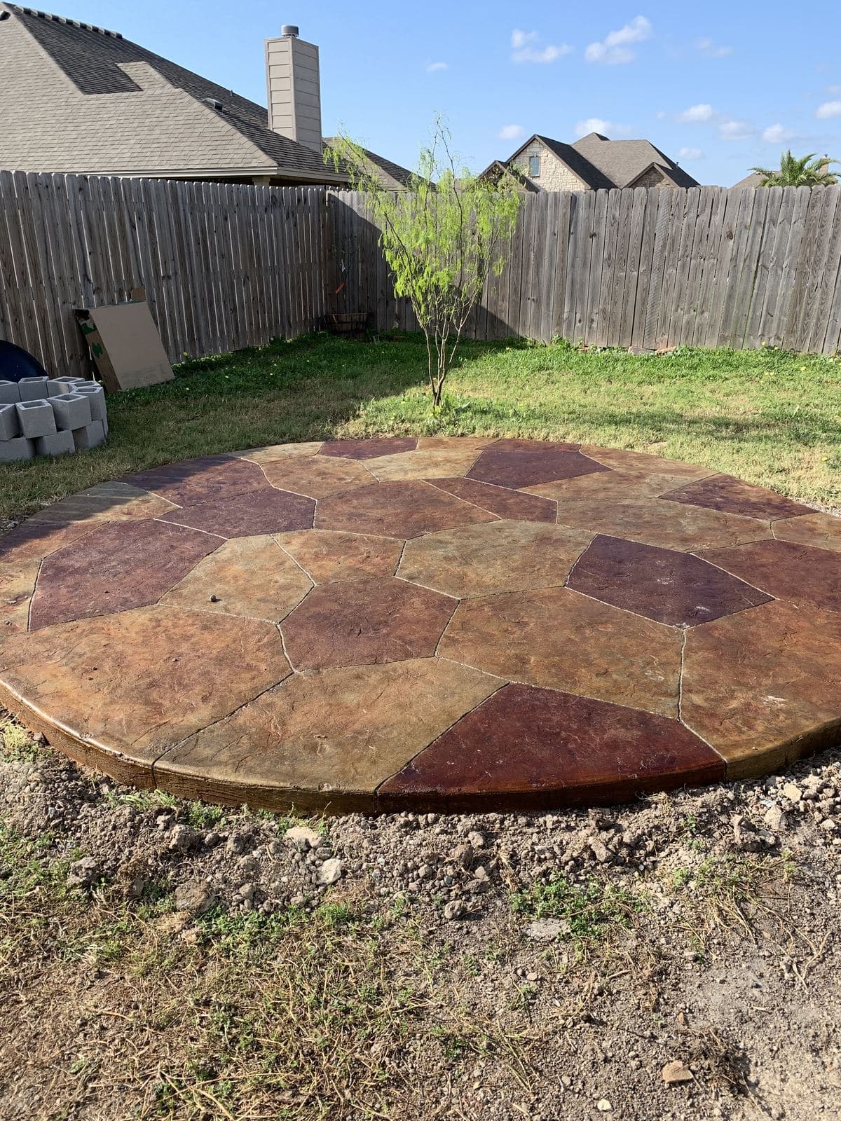 Round stamped flagstone patio in rust and tan in a fenced back yard